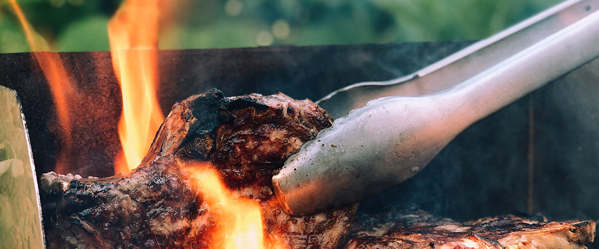 Meat being turned on a braai with flames