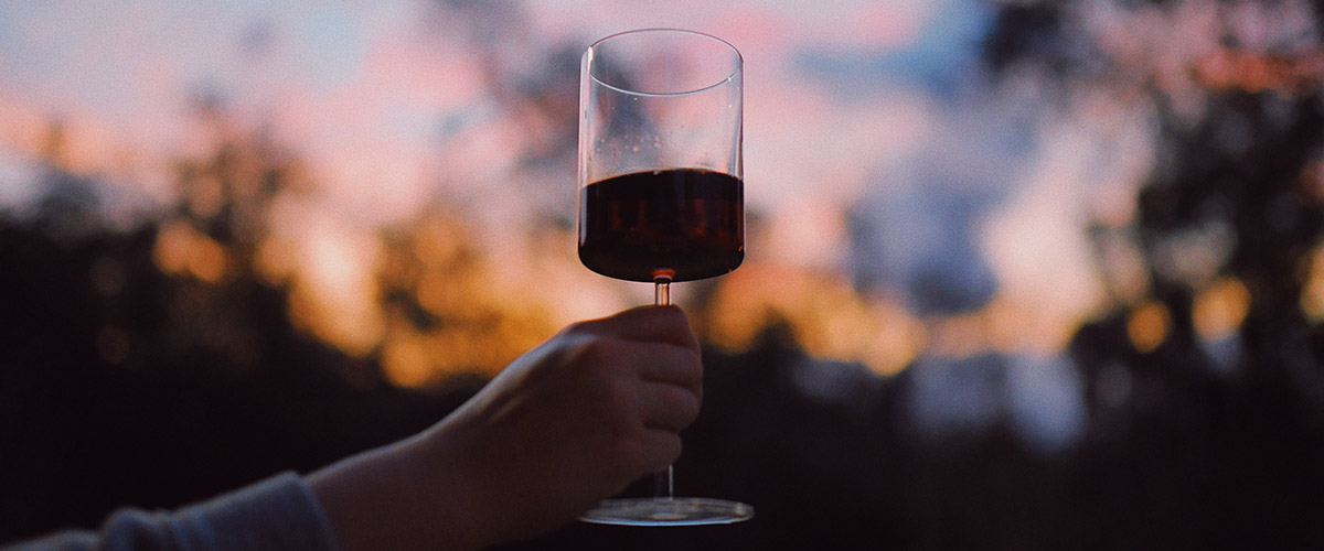 Hand holding up a glass of red wine before doing virtual wine experiences