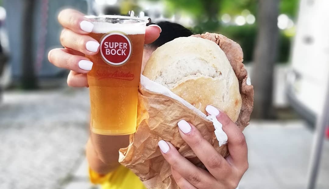 Woman holding bifana sandwich and Portuguese beer